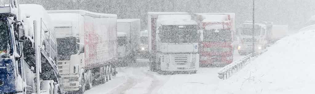 Mehrere LKW kämpfen sich bei starken Schneefall über eine Straße.