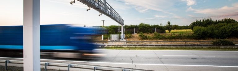 Fahrender LKW auf einer Autobahn unter einer LKW-Maut-Brücke