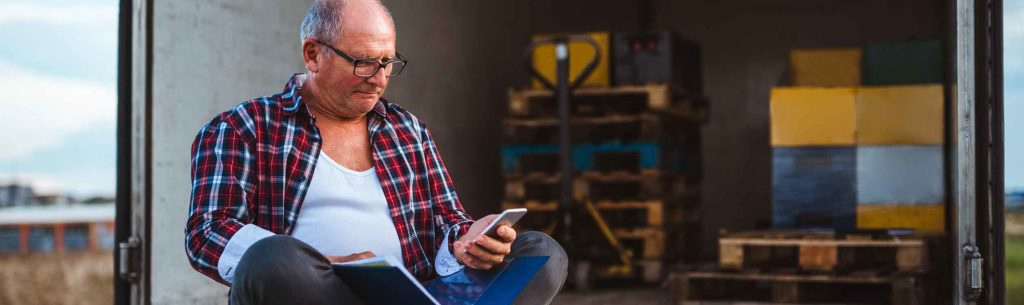 LKW-Fahrer sitzt auf der Ladefläche mit Rechnungen und schaut auf sein Handy