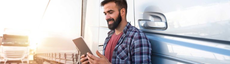 Truck driver stands in front of truck and types on his tablet