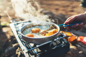 Person cooks fried eggs in nature camping outdoors, cooker prepare scrambled eggs breakfast picnic on metal gas cooker, tourism recreation outside; camping lifestyle