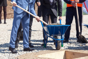 Männer im Anzug füllen Sand mit einem Spaten zur Grundsteinlegung