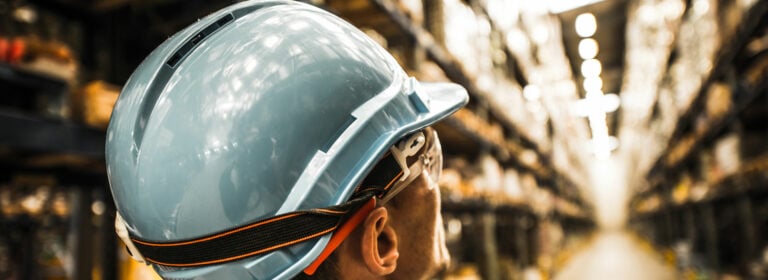 Symbol image about safety for workers. Man with a safety hero on his head looks in a high bay warehouse