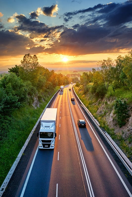 How digital transformation drives sustainability in logistics, Three trucks on a road before sunset