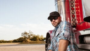 Alternative Truck driver with trucker cap in front of his truck