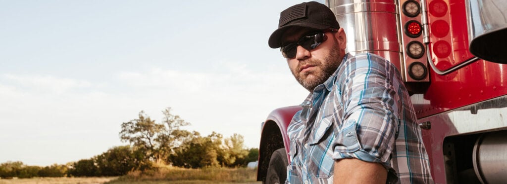 Truck driver with trucker cap in front of his truck