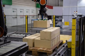 Industrieller Roboterarm beim Beladen eines Kartons auf einem Förderband in einer Produktionslinie